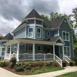 A two-story blue Victorian-style house with a wraparound porch and two turrets.