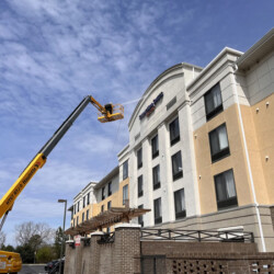 A worker in a boom lift pressure washes the exterior of a multi-story hotel.