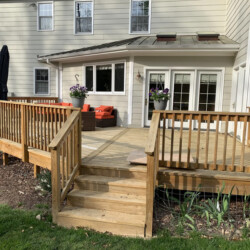 A wooden backyard deck with stairs, orange patio furniture, and hanging flower baskets against a house.