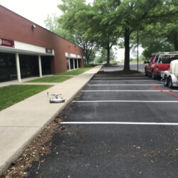 A surface cleaning robot on a sidewalk next to a red truck towing a water tank trailer.
