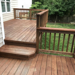 A two-level wooden deck attached to the side of a house with steps connecting the tiers.