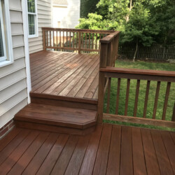 A freshly stained wooden deck with railings and a single step leading to an upper level.