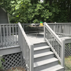 Gray wooden deck with stairs and a lattice skirt, featuring a small table with a toy on top.