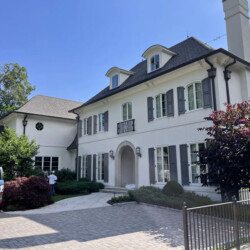 A white two-story house with dark gray shutters and a stone paver driveway.