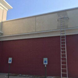 A tall ladder leans against the exterior wall of a building with two accessible parking signs in front.