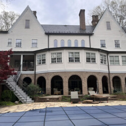 Back of a large white house with a brick ground-floor arcade and a pool with a blue cover.