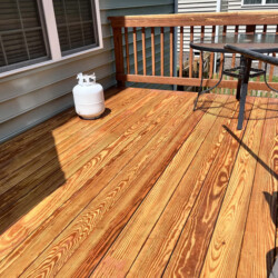 A wooden deck featuring a propane tank, a glass-topped table, and a partial view of patio chairs.