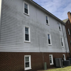 Two-story building with white horizontal siding above a red brick base, showing vertical streaks of gray staining.