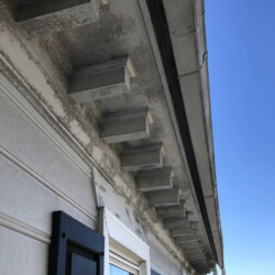 Exterior house roofline with peeling paint on decorative eaves brackets.