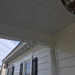 White building exterior with a column, overhanging porch roof, and black window shutters.