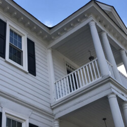 White two-story house with black shutters and a covered porch supported by columns.