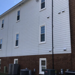 Side of a two-story building with white siding, brick base, multiple windows, and several HVAC units.