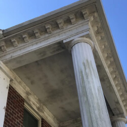 Low-angle view of a building’s white classical column and decorative cornice against a clear blue sky.