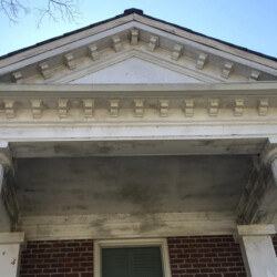 A white pediment with decorative molding supported by two fluted columns over a brick house entrance.
