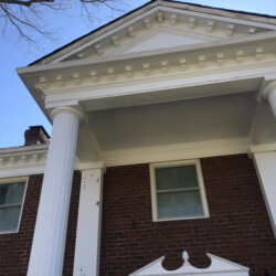 A brick house exterior featuring a pediment roof supported by two large white columns.