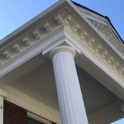 The white column and decorative cornice of a neoclassical porch against a blue sky.