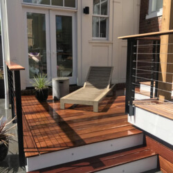 A wooden deck with a lounge chair, steps, and a cable railing outside a house.