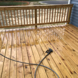 A wet wooden deck with a power washer nozzle resting on the surface.
