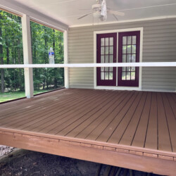 A brown wooden deck with white railings, looking out toward a forest, with two plastic water bottles on the rail.
