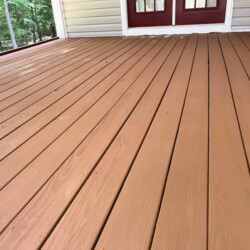 A wooden deck with light brown stain leading to a house with red double doors.