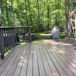 A person staining a wooden deck with a long-handled roller in a backyard.