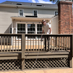 A man in a hat stands on a wooden deck next to a house with a brick chimney.