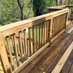 A wooden deck with a railing overlooking a backyard and trees.