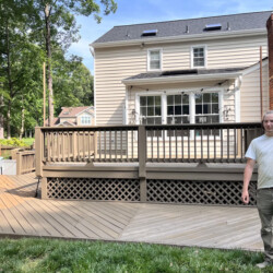 A young man stands on a large, multi-level wooden deck attached to the back of a house.