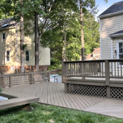 A wooden backyard deck with railings extending from a two-story house.