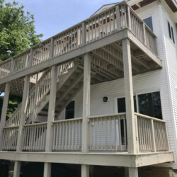 A two-story wooden deck with stairs attached to the back of a white house.