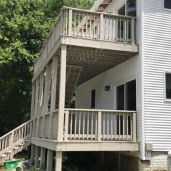 A two-story wooden deck with stairs attached to the side of a white house.