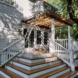 A tall ladder leaning against the side of a house on a wooden deck with a pergola.