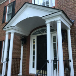 Brick house entrance featuring a white portico supported by columns over a black front door.