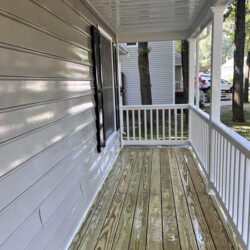 A freshly washed wooden porch with white railings and beige siding.