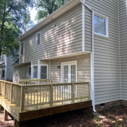 A new wooden deck attached to the back of a light-gray two-story house.