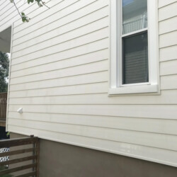 Exterior wall of a house with white horizontal siding, a single window, and a wooden deck.