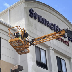 A worker in a lift bucket performing maintenance on a SpringHill Suites hotel sign.