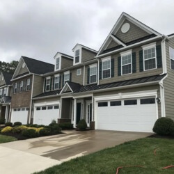 A row of multi-story townhouses with tan siding, peaked roofs, and white garage doors.