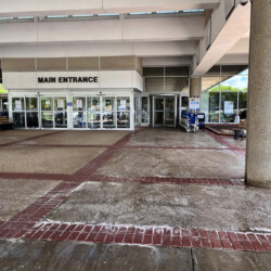 The main entrance of a building with sliding glass doors, a large concrete pillar, and rows of seating.