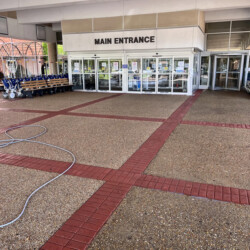 Main entrance of a building with rows of wheelchairs and a garden hose on the pavement.