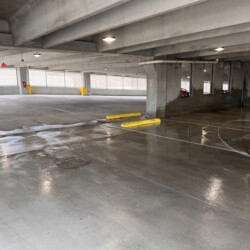An empty concrete parking garage level with a single orange traffic cone in the foreground.