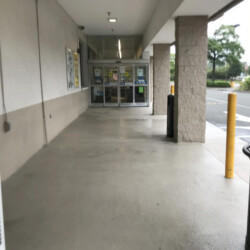 A covered sidewalk leading to the sliding glass entrance of a store.