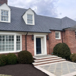 A red brick house with a dark roof, a front door, and a stone patio.