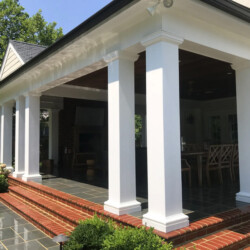 Covered stone patio with white columns and brick steps.