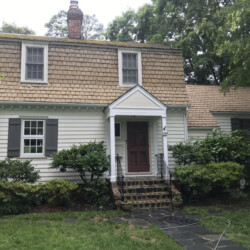 Two-story house with cream siding, a shingled gambrel roof, and dark shutters.