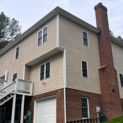 A two-story house with tan siding, a red brick base, and a chimney.