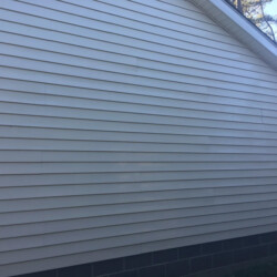 Side view of a house exterior with light-colored horizontal siding and a dark masonry foundation.